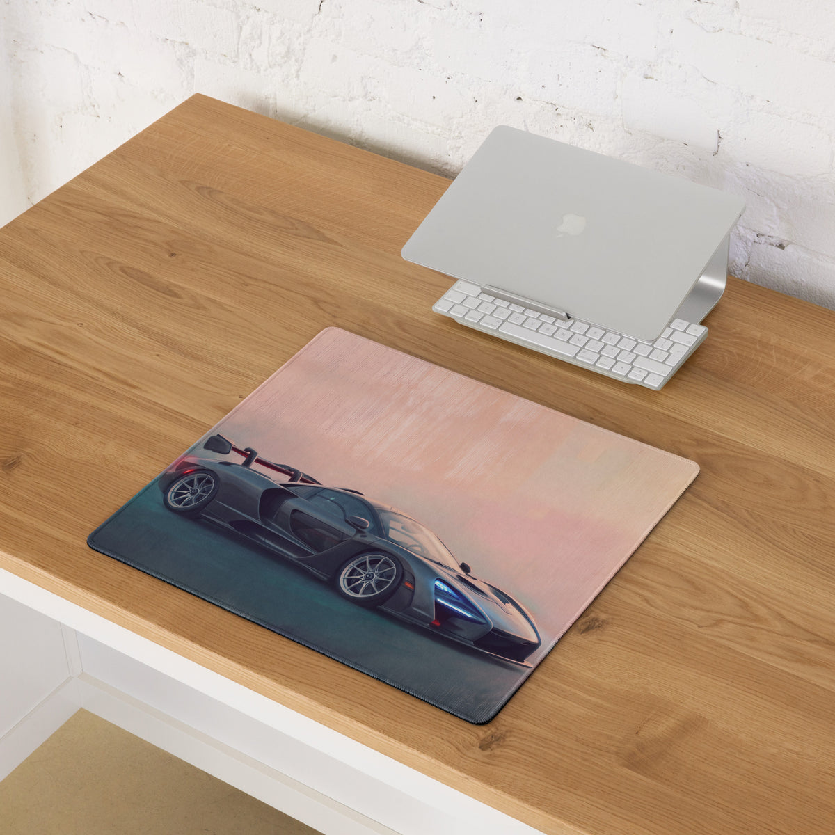 Rectangular McLaren Senna inspired carbon stealth desk mat with dark gray sports car on soft pink teal gradient background