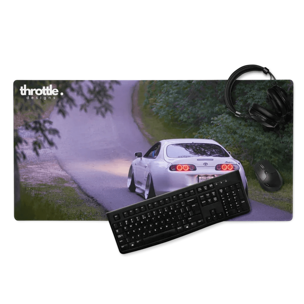 Extended gaming mouse pad with white Toyota Supra Mk4 rear view on winding road under trees.