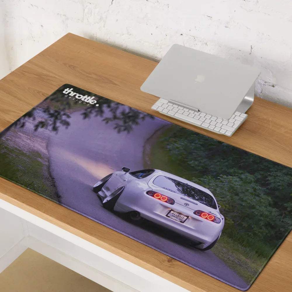 Large gaming mouse pad featuring a rear view of a silver Toyota Supra MK4 on a winding road surrounded by trees.
