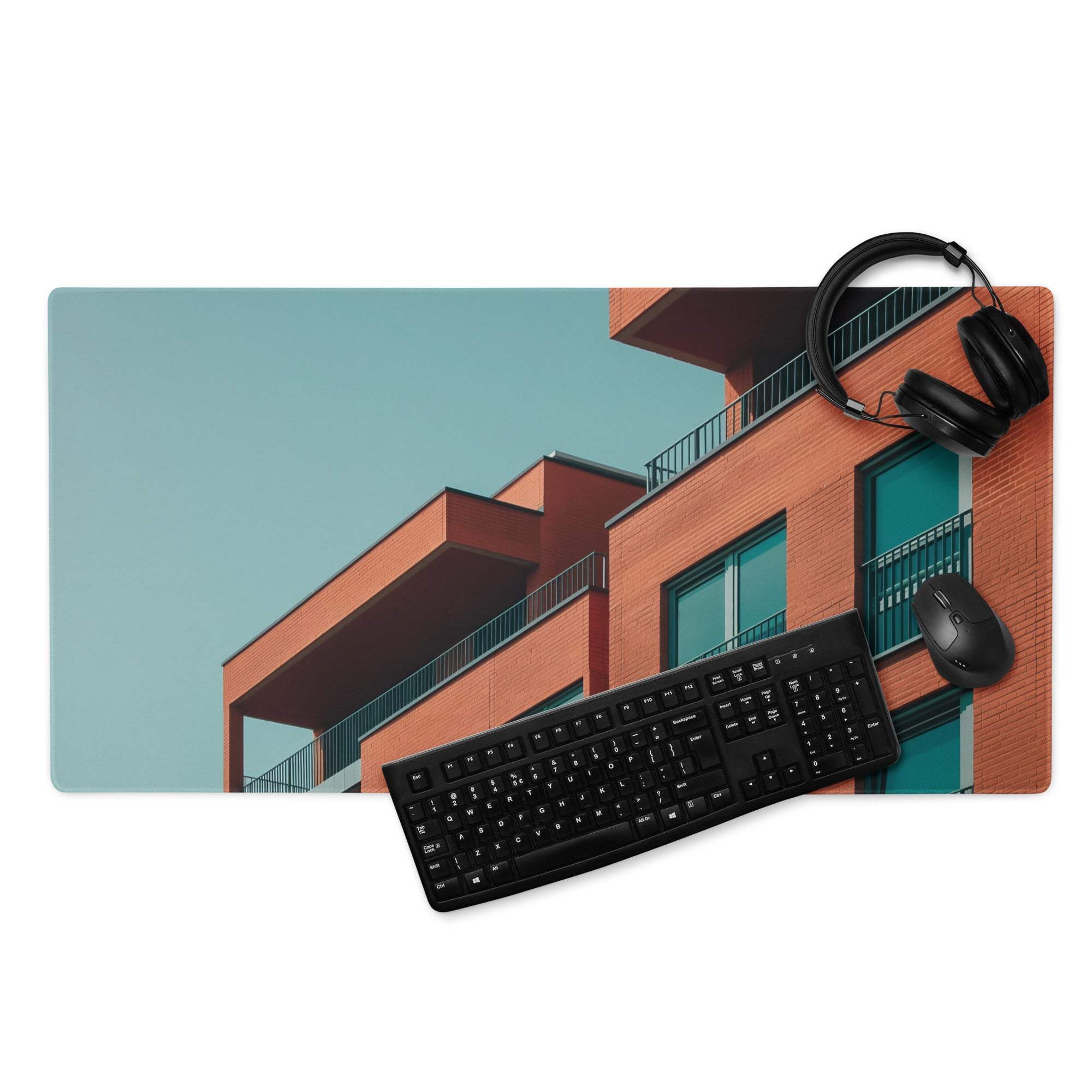 Sleek large edge-stitched gaming mouse pad with orange brick building, teal windows, headphones and keyboard