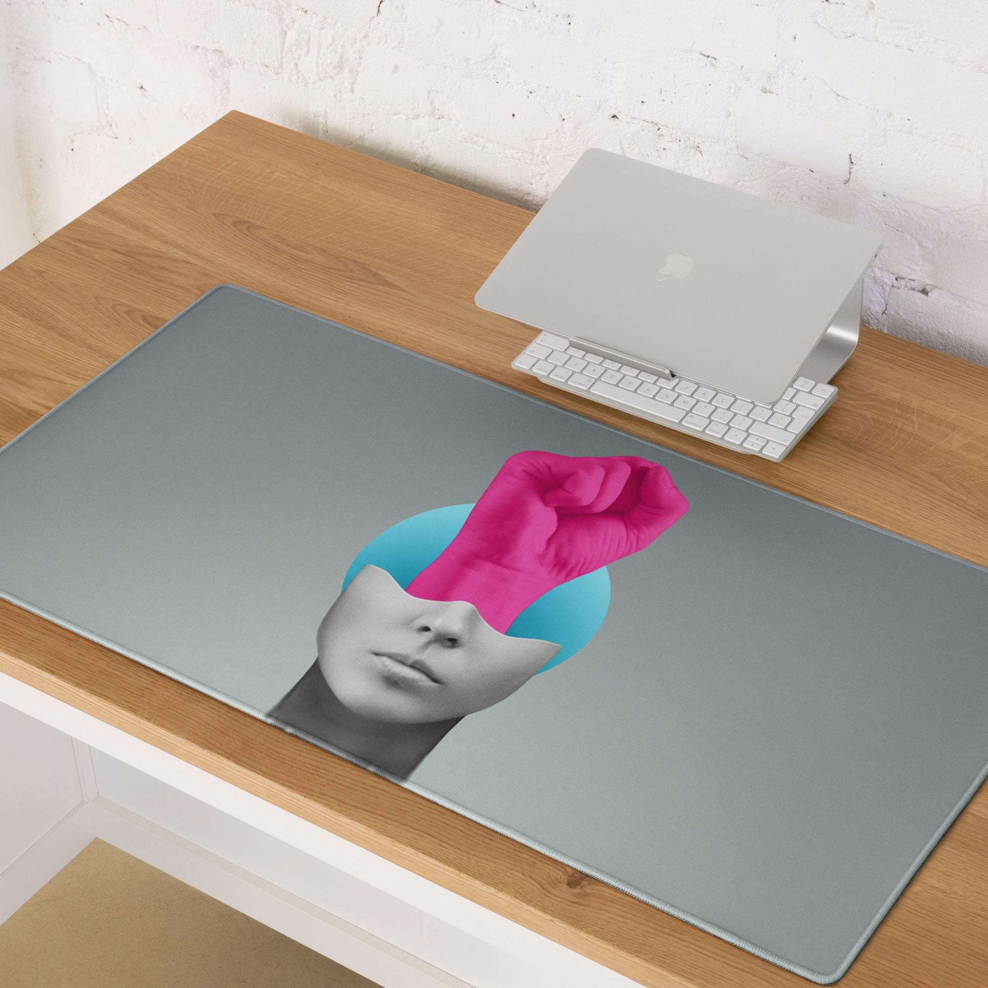 Sleek gray rectangular desk pad featuring a pink hand portrait with a vibrant pink fist on a teal background