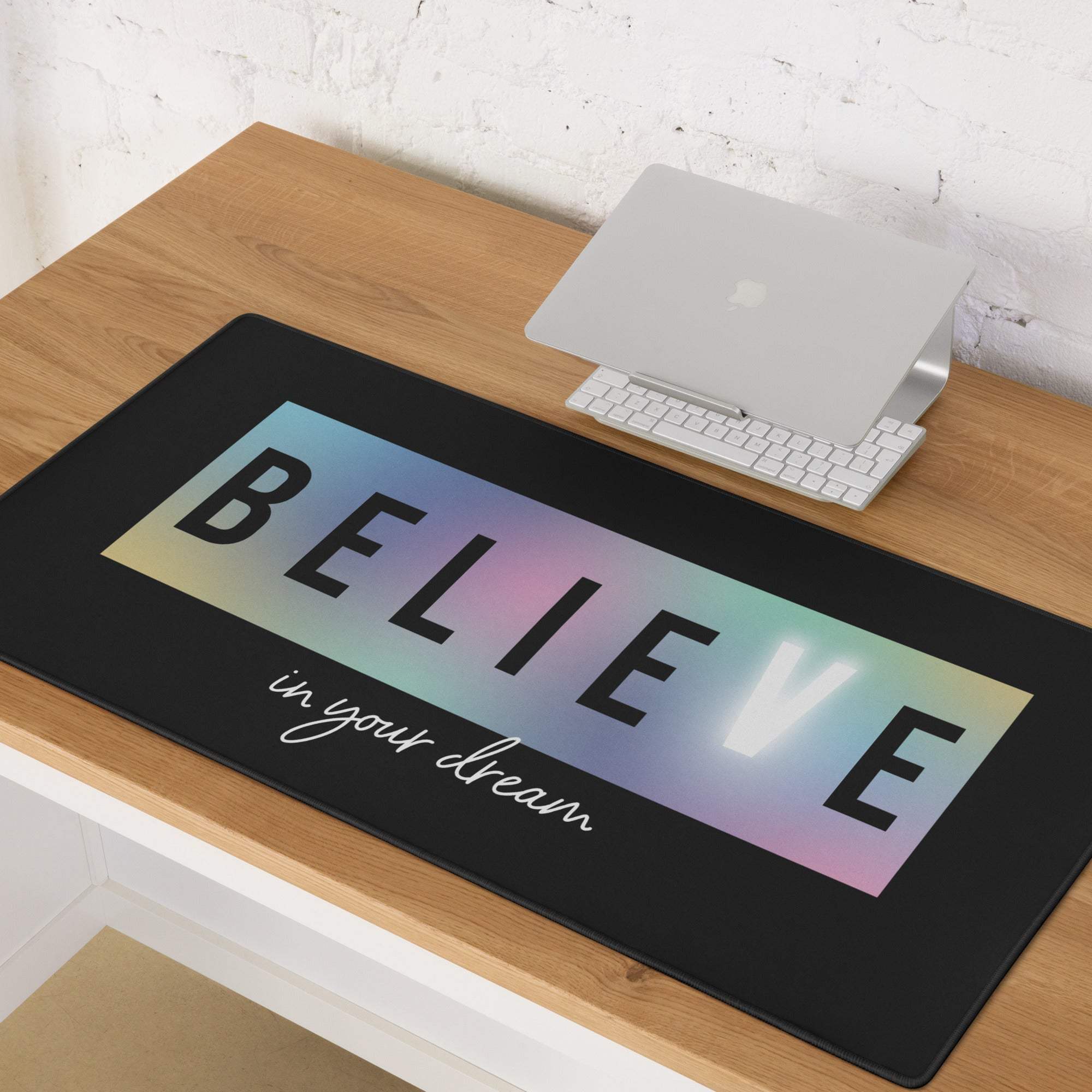 Black rectangular mousepad with rainbow gradient background featuring bold believe and white cursive in your dream text