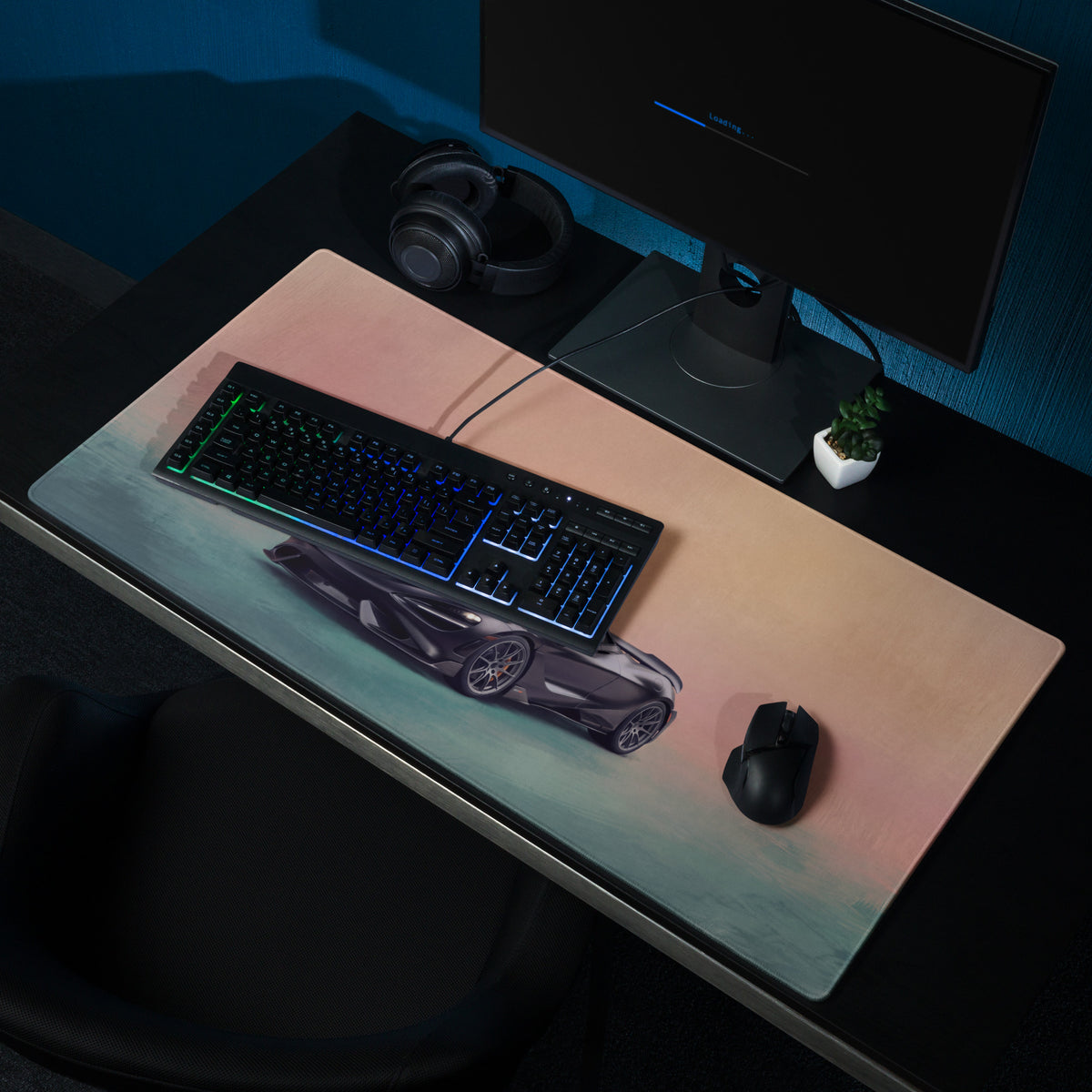 A sleek rectangular low-friction cloth desk mat with a dark gray sports car graphic on a peach to teal gradient background