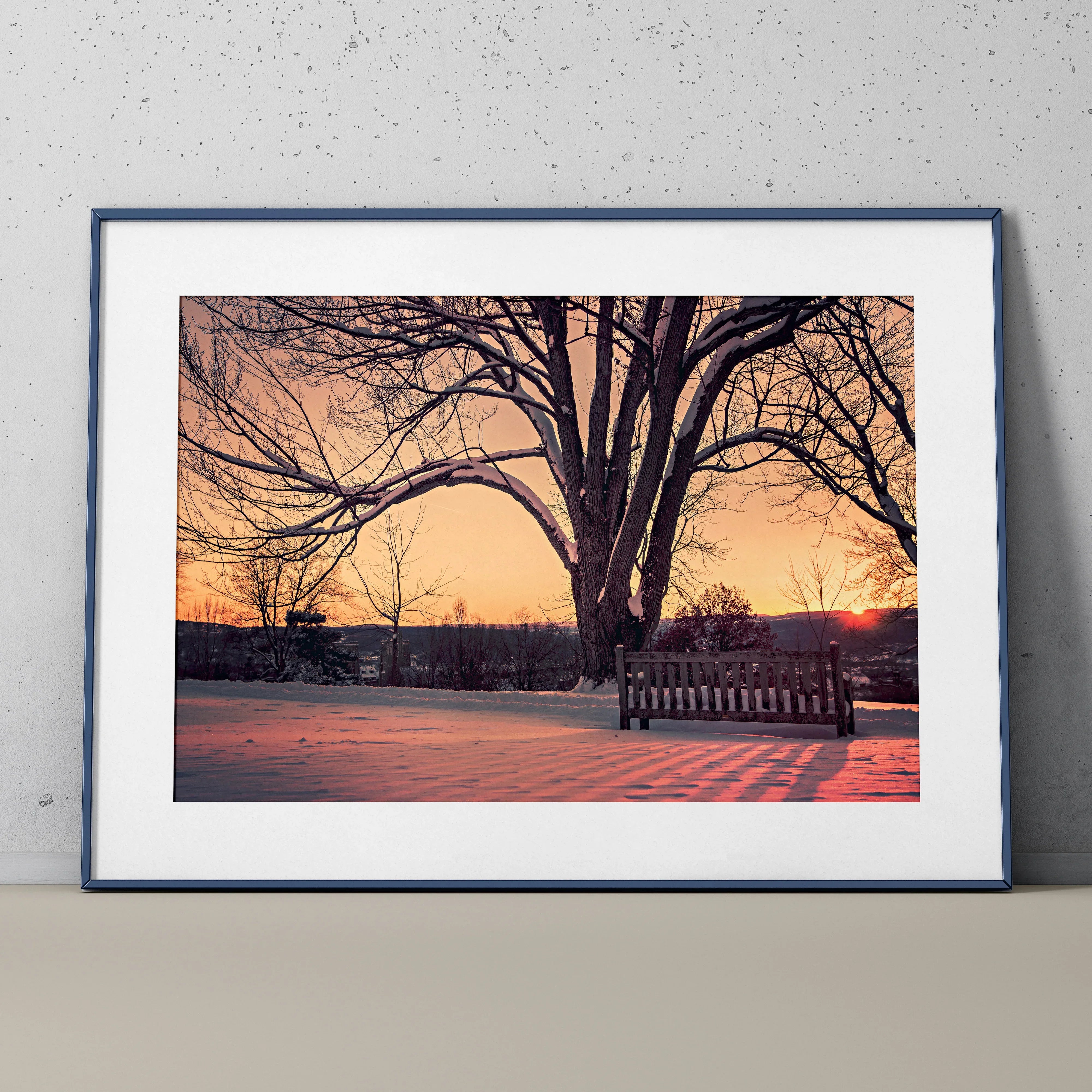 Serene snowy landscape wall art poster with large bare tree and wooden bench at sunset.