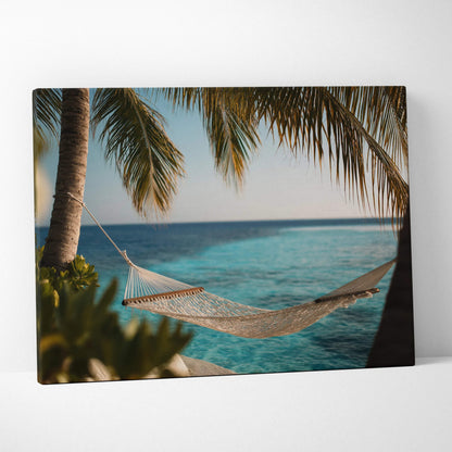 Canvas wall art of a hammock between palm trees over clear turquoise ocean waves at sunset.