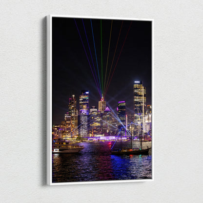Vertical canvas wall art of illuminated urban skyline with colorful laser lights over water at night.