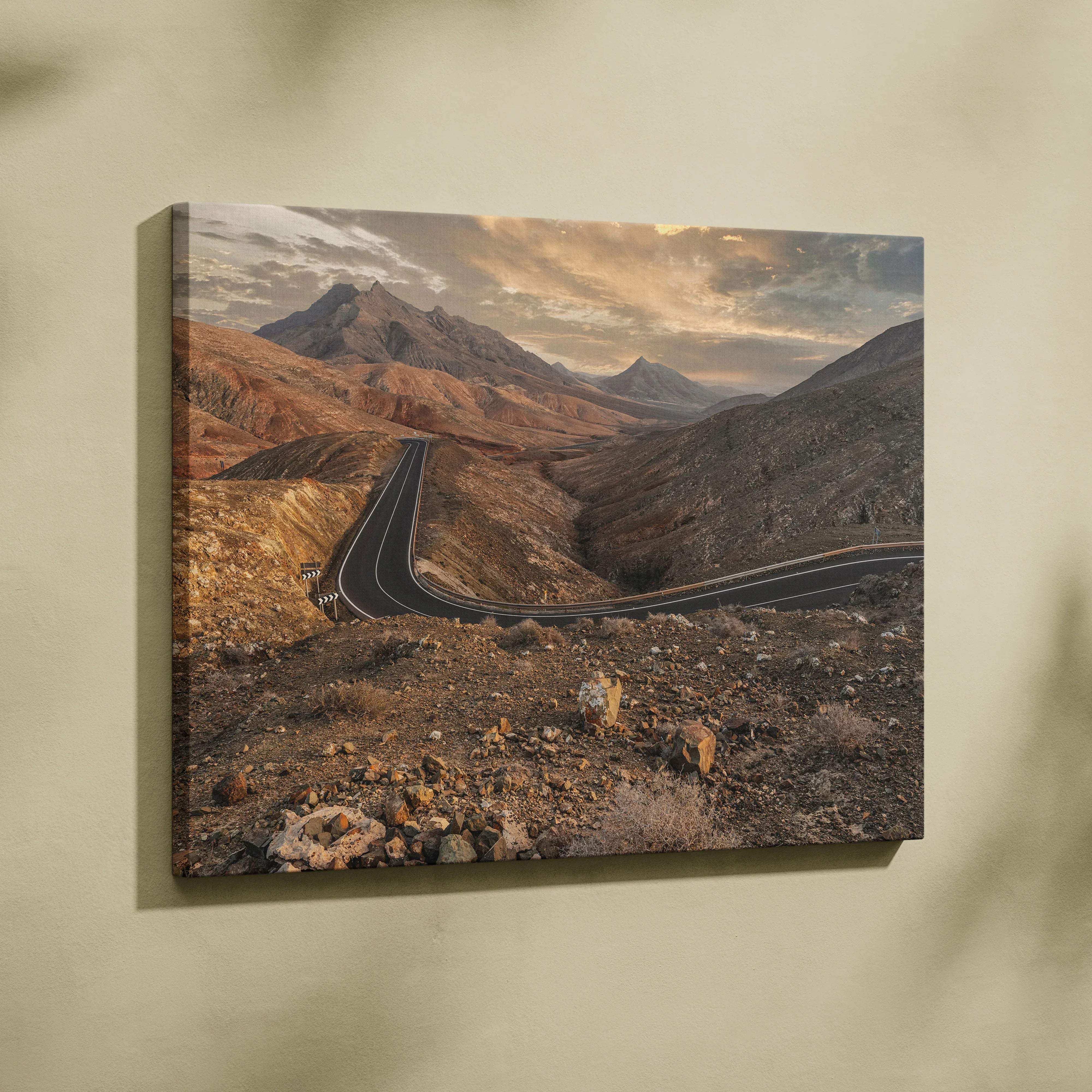 Rectangular canvas wall art featuring a winding asphalt road through desert mountains in warm earth tones