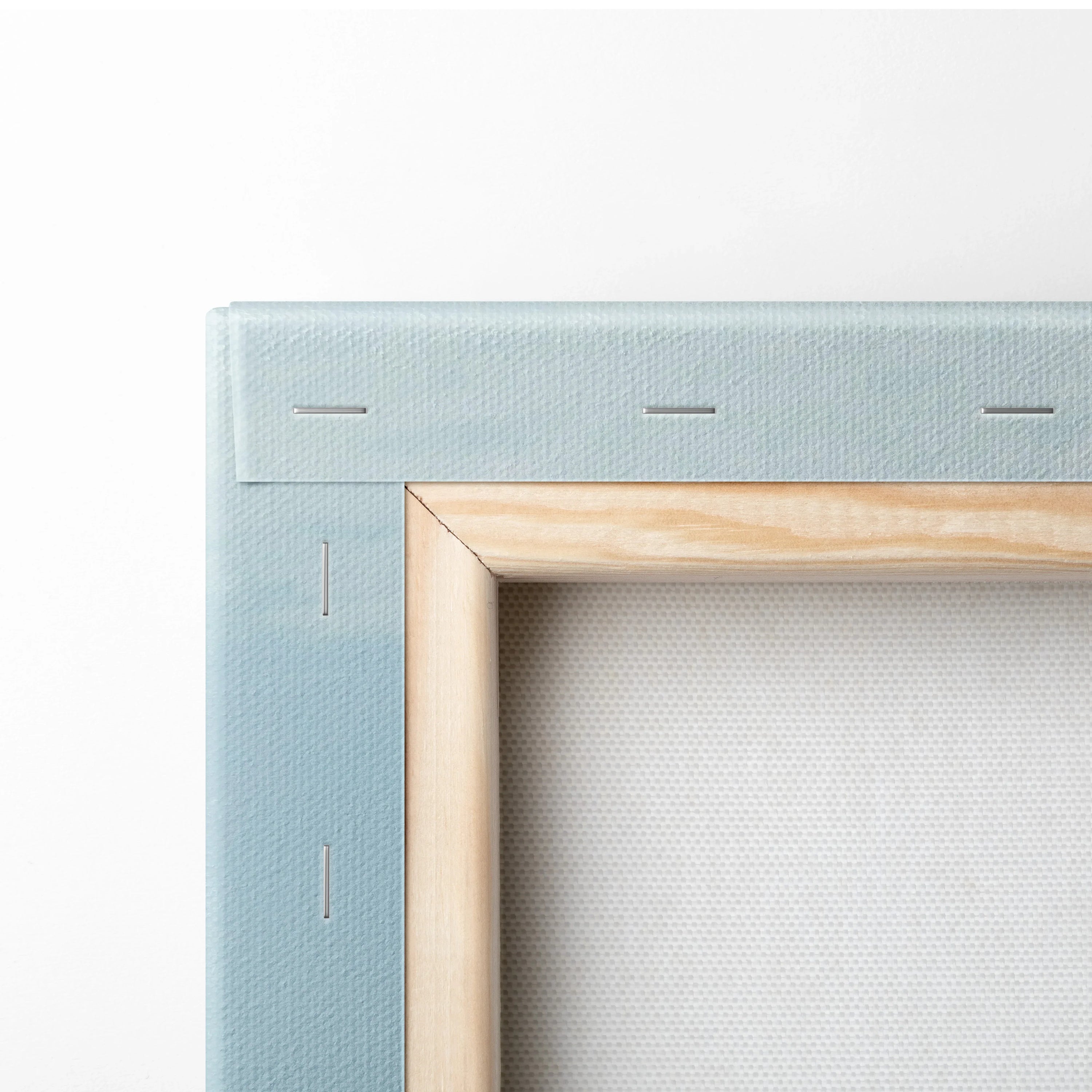 Close-up of canvas wall art corner showing light wood frame and blue fabric backing with stapled edges.