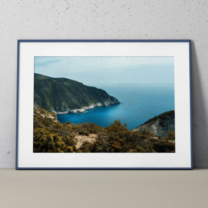 Framed poster wall art of ocean bay with rugged mountain cliffs under clear blue sky.