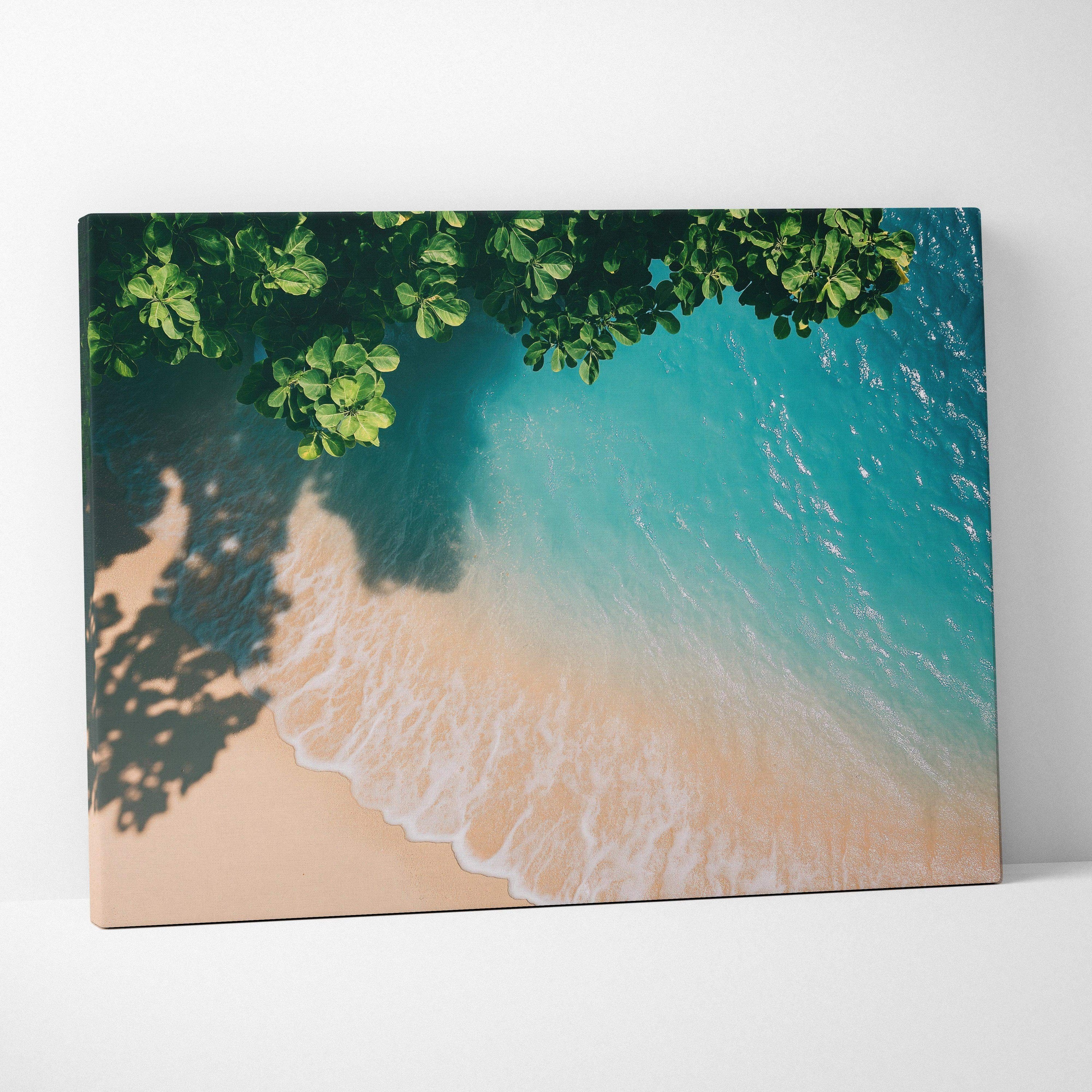 Canvas wall art of tranquil ocean waves gently washing onto sandy beach under leafy green tree shadows.