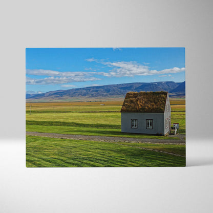 Canvas wall art featuring a solitary rustic building surrounded by green fields under a blue sky.