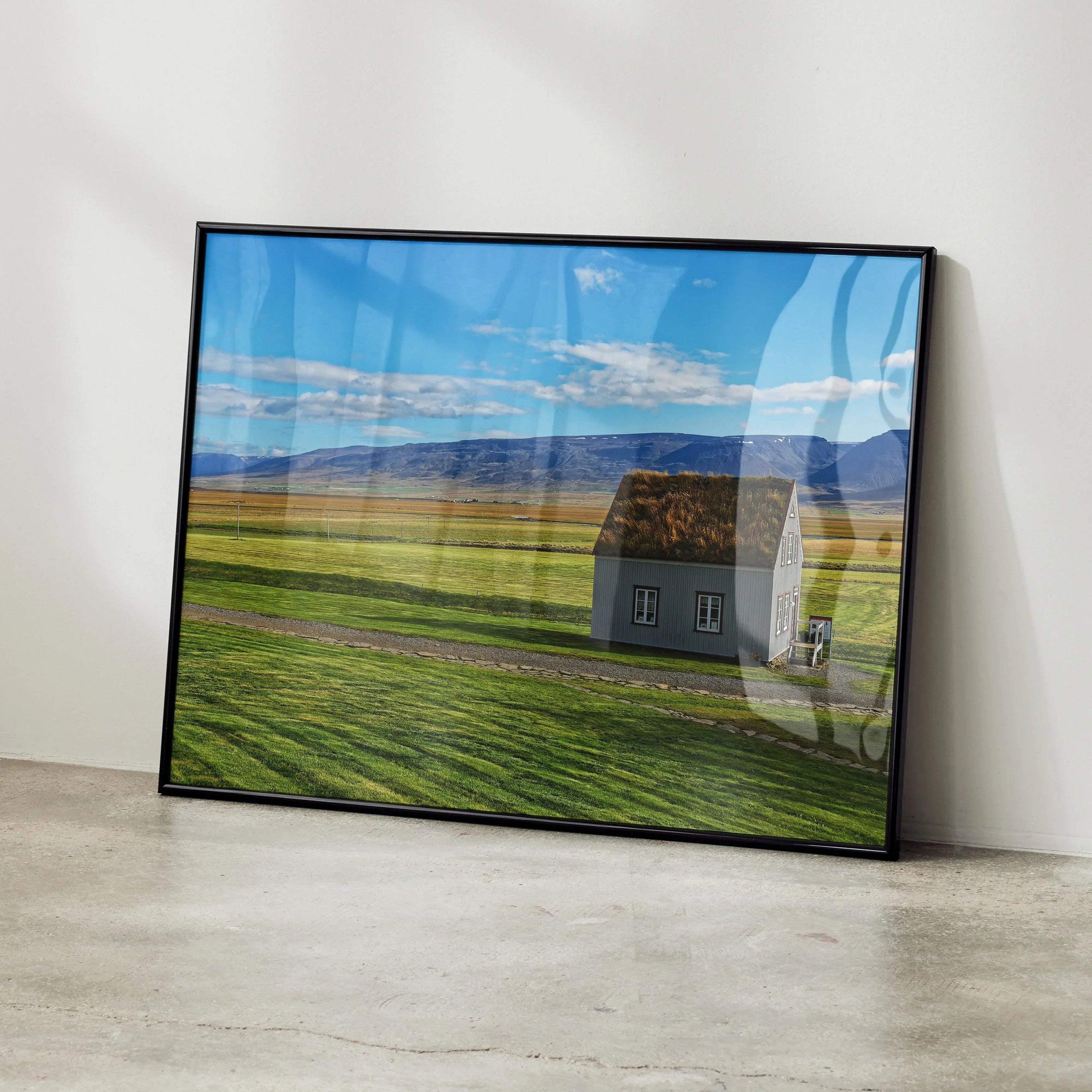 Modern architectural building wall art poster featuring a small house in a vast green field under a blue sky with clouds,.