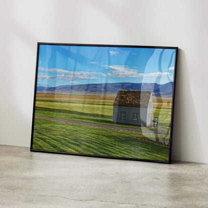 Modern architectural building wall art poster featuring a small house in a vast green field under a blue sky with clouds,.