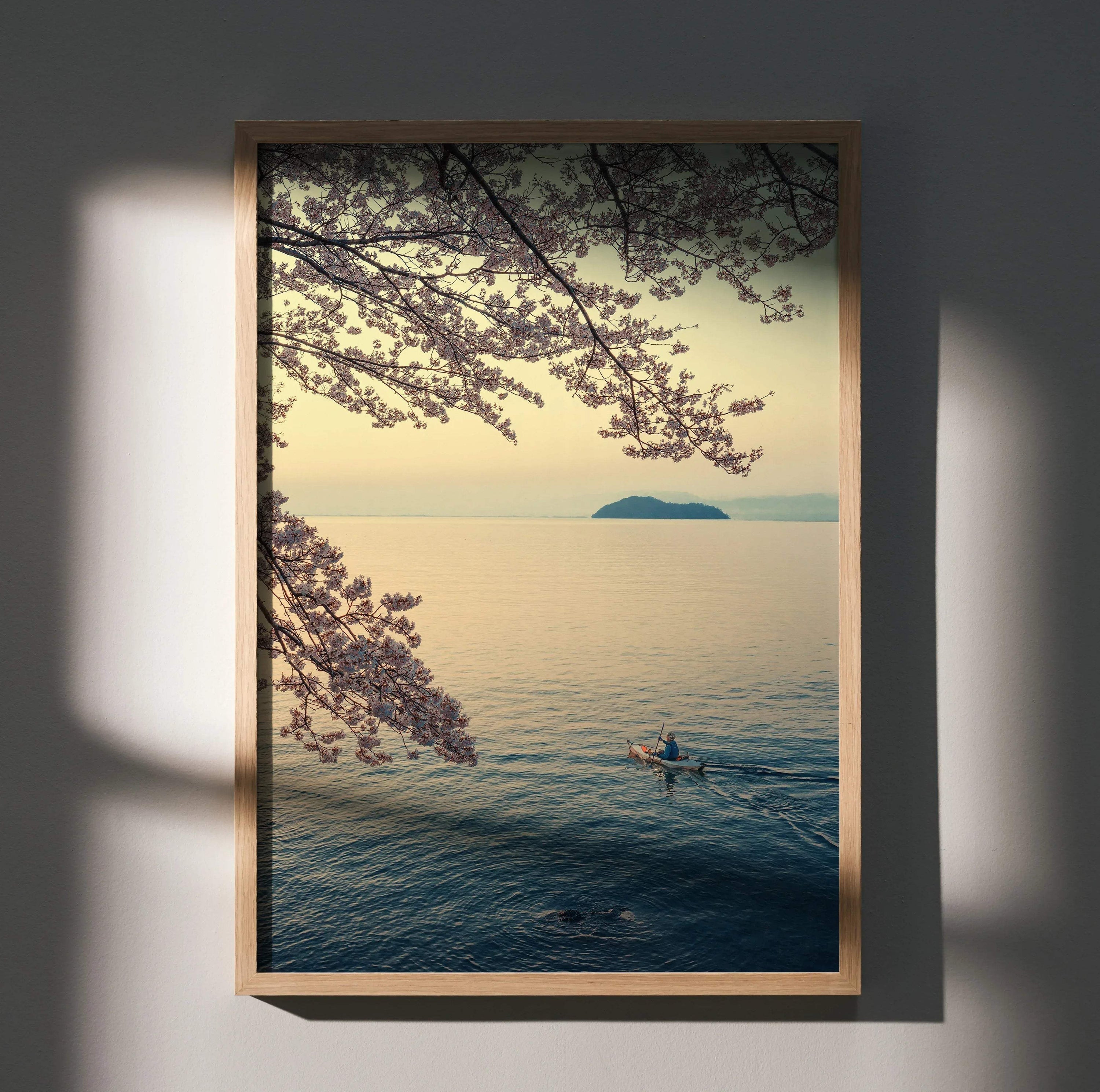 Vertical wall art poster of serene ocean scene with cherry blossom branches and lone kayaker at sunset.