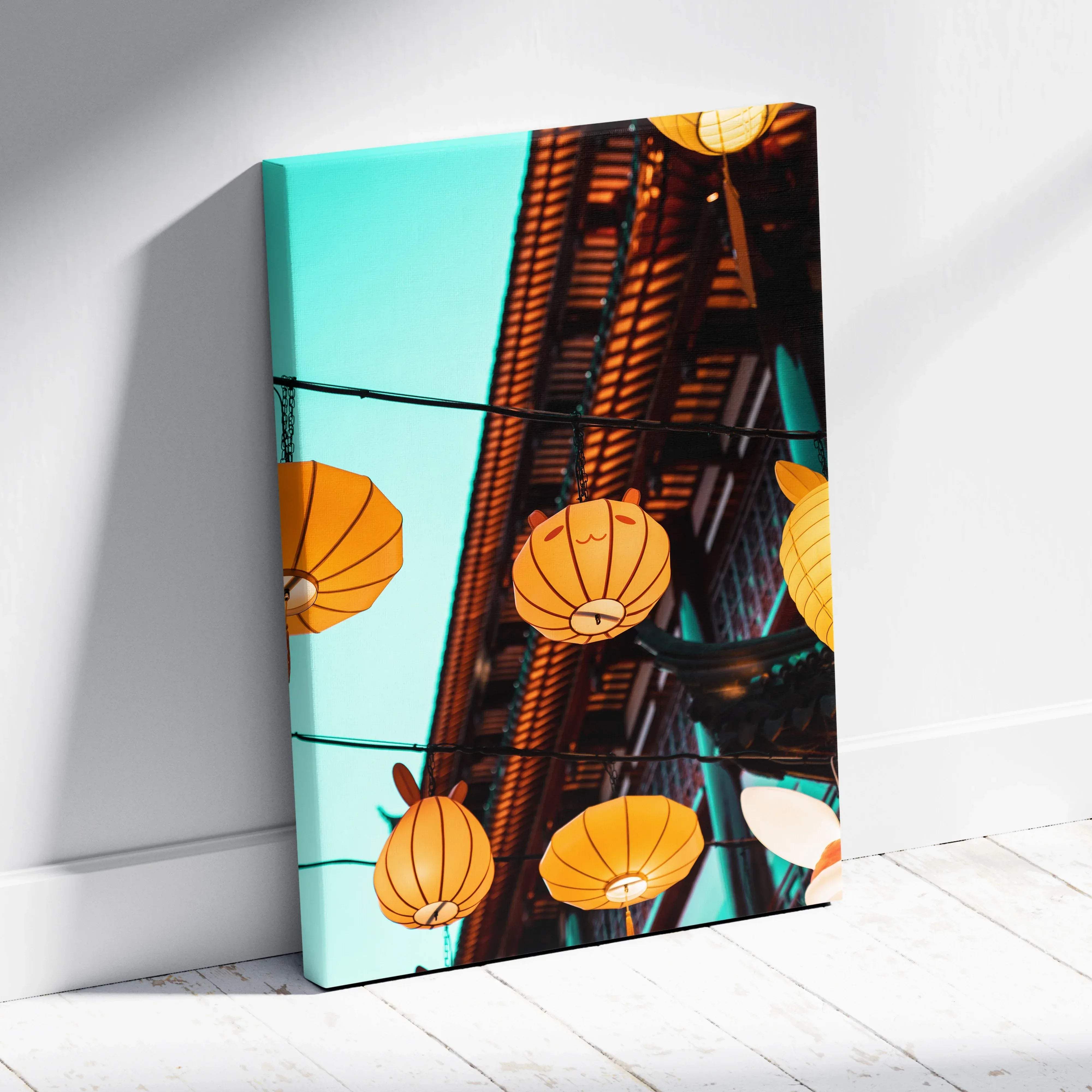 A vibrant canvas wall art print featuring glowing orange paper lanterns over historic wooden architecture with teal sky