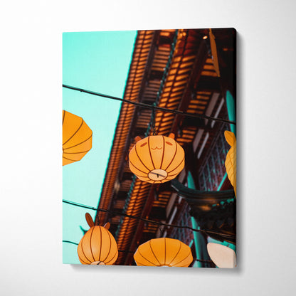 Vertical canvas wall art featuring orange lanterns hanging against a turquoise sky and traditional wooden architecture.