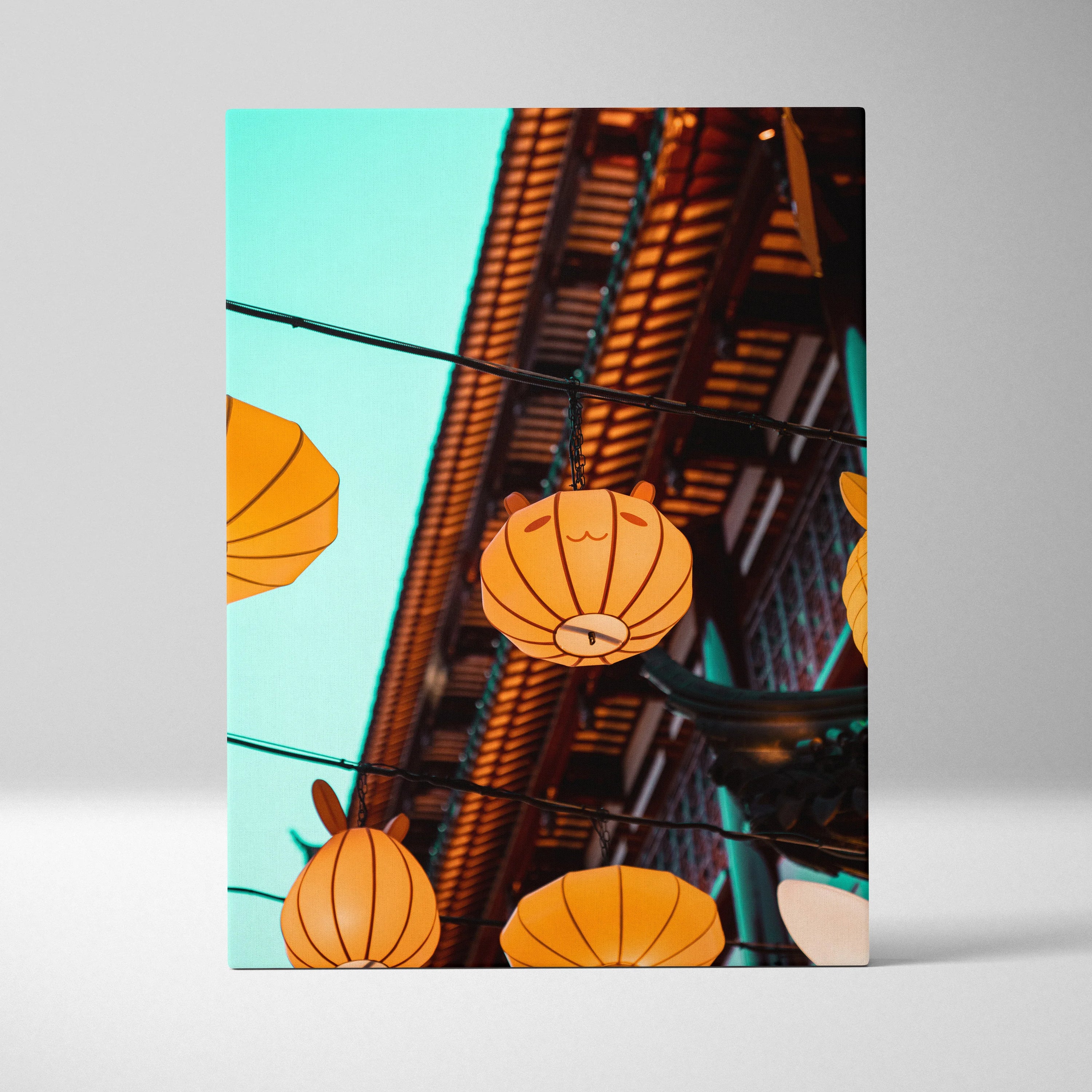 Vertical canvas wall art featuring glowing orange lanterns against a clear blue sky, urban architectural backdrop.