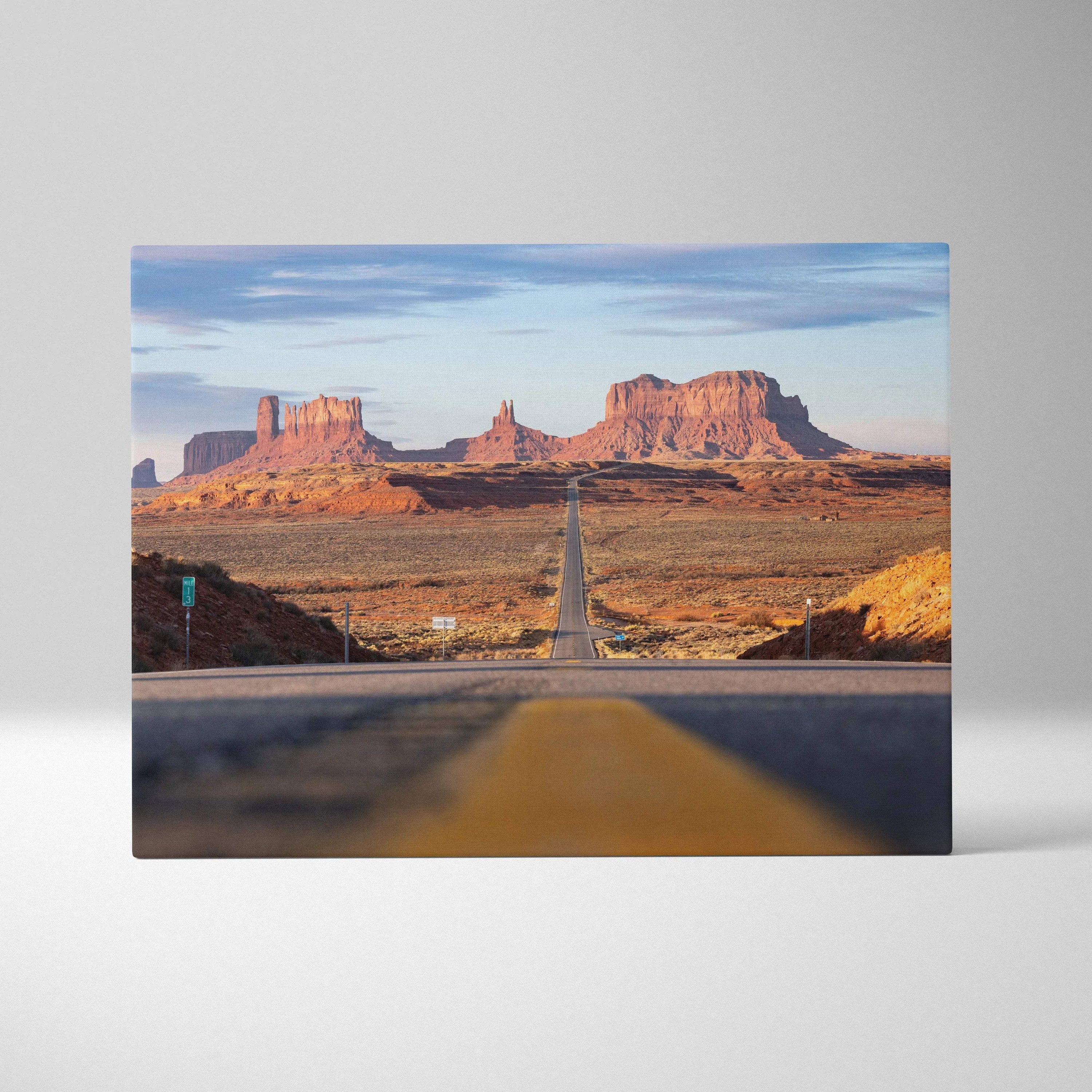 Desert landscape wall art canvas featuring a long road leading to red rock mesas under blue sky.