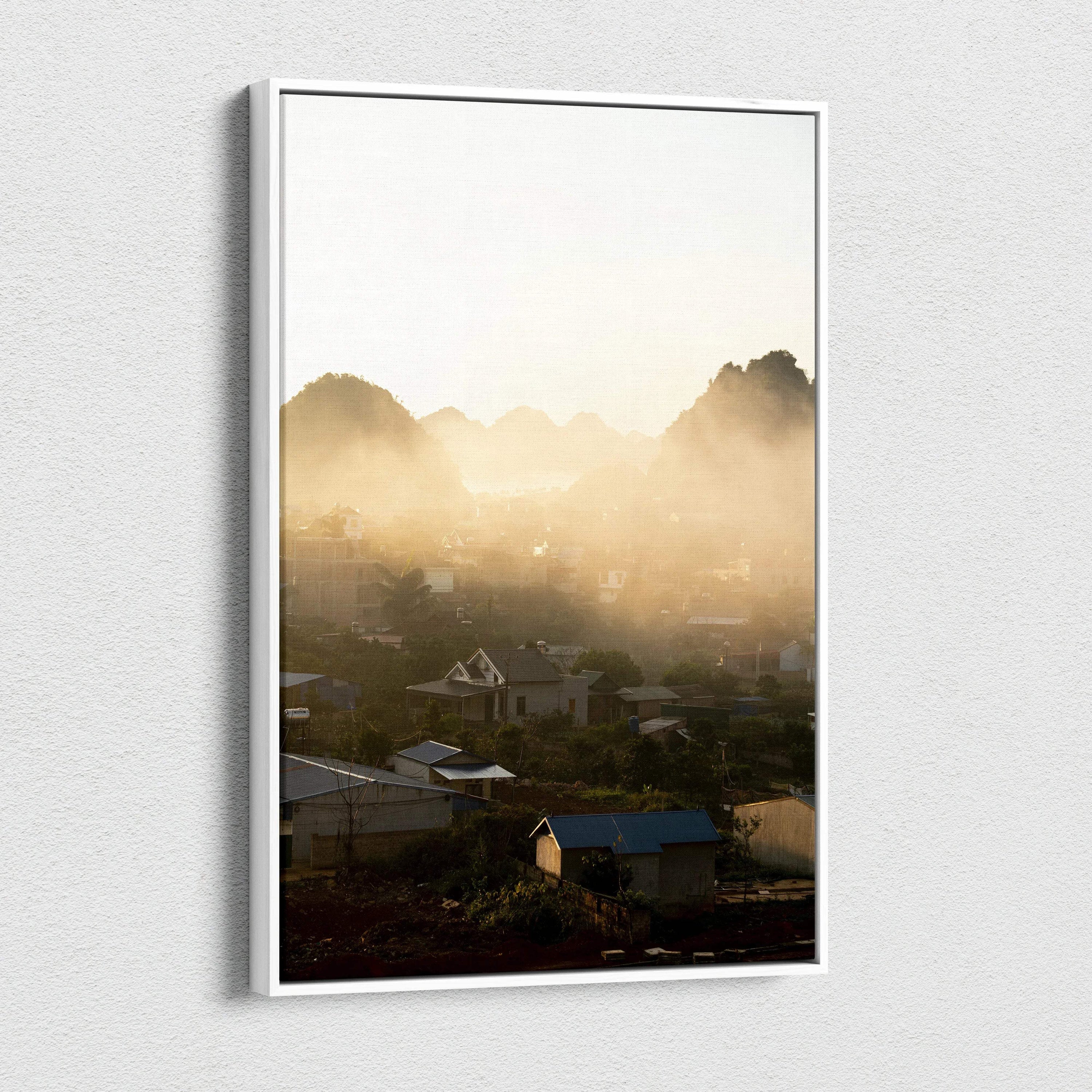 Vertical canvas wall art featuring a misty mountain landscape with soft sunlight and village rooftops.