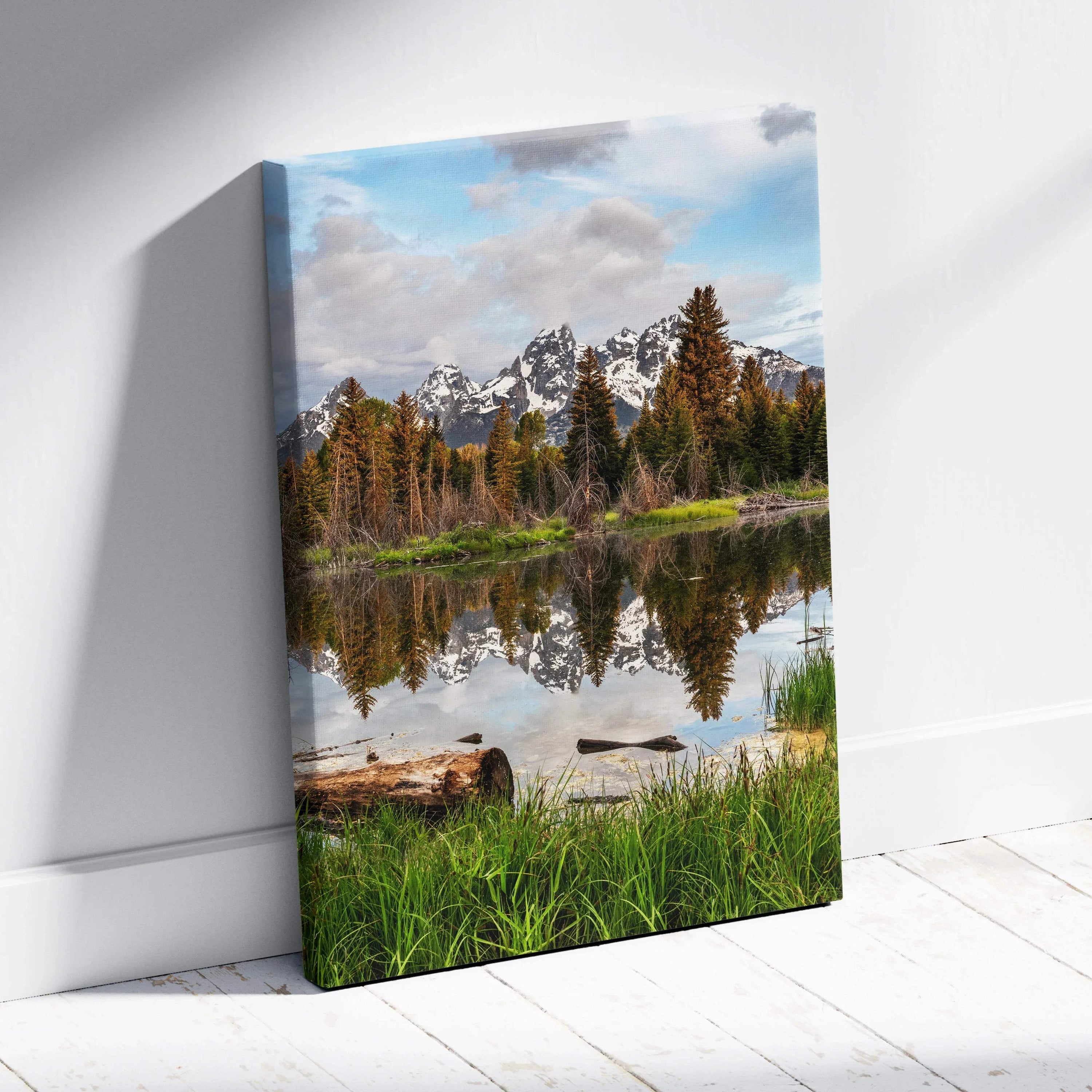 Vertical canvas wall art featuring majestic snow-capped mountains reflected in a calm lake with green grass and pine trees.