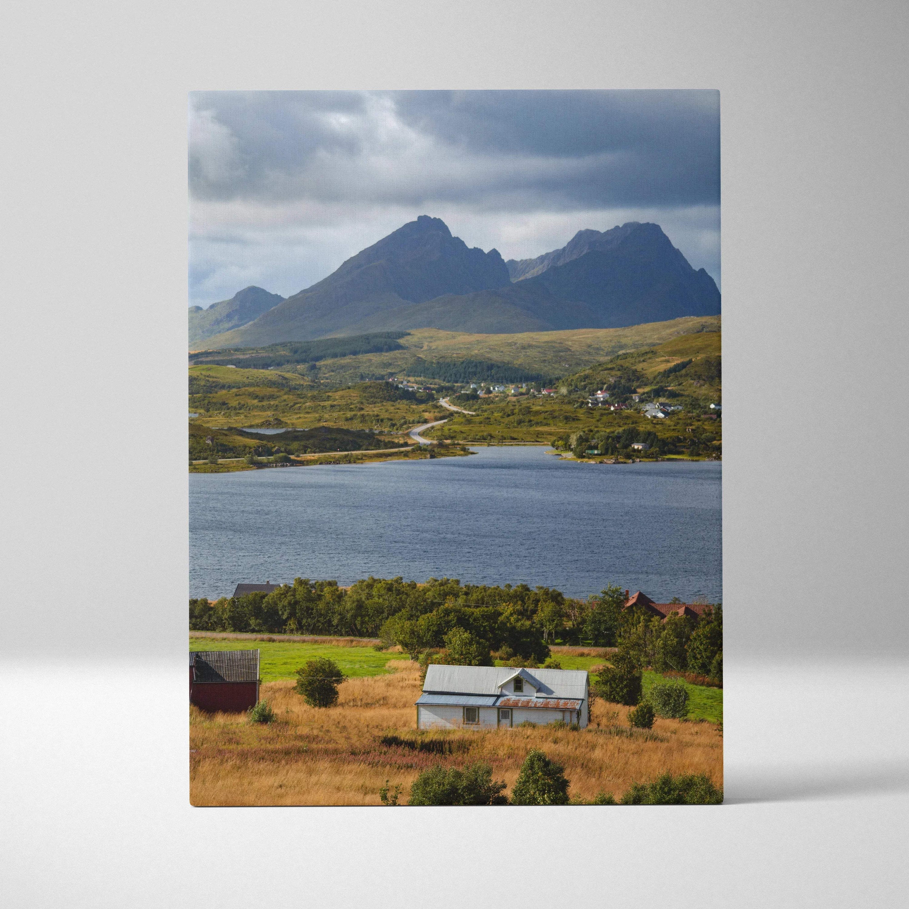 Canvas wall art featuring majestic mountains under cloudy sky over lake and rustic house in foreground.