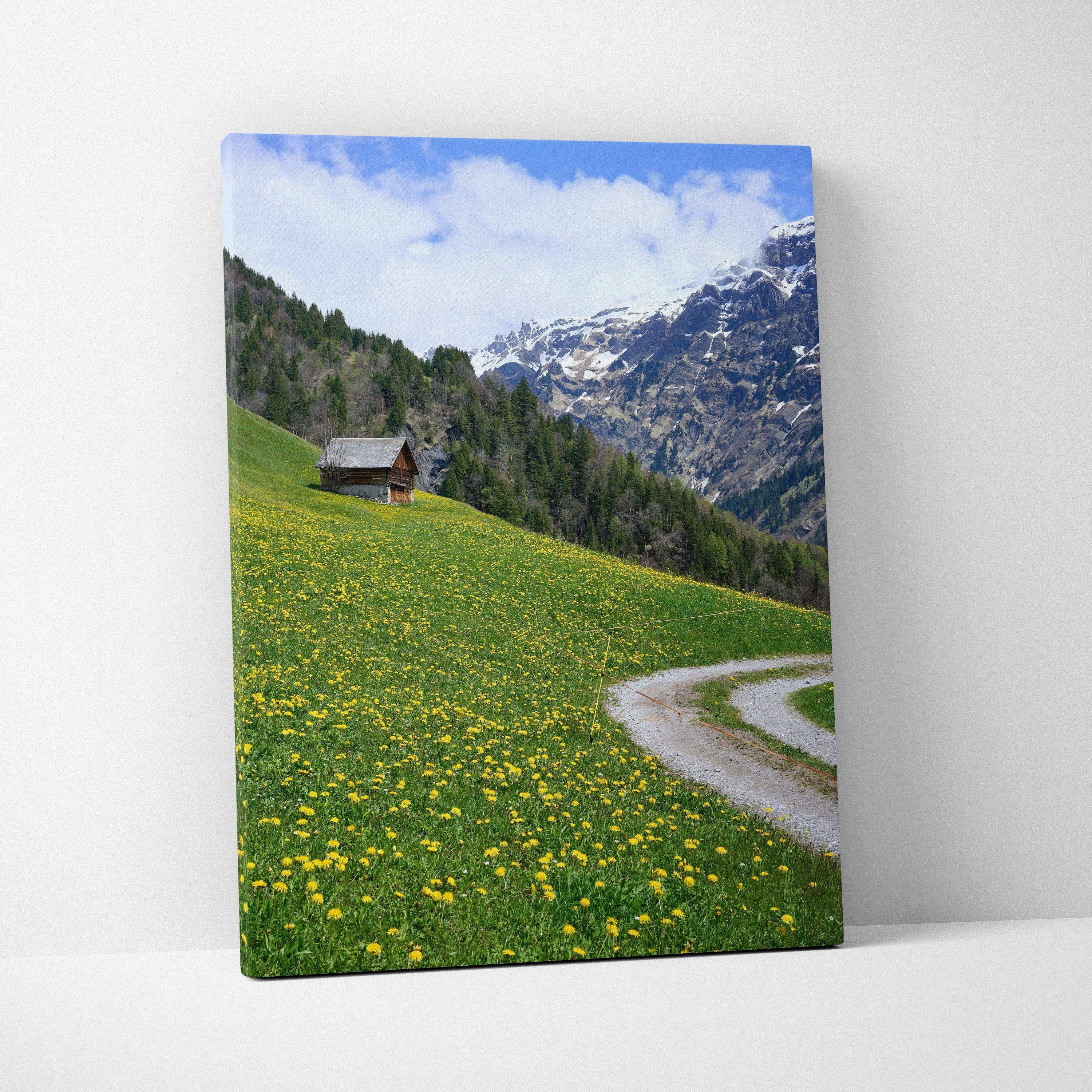 Vertical mountain landscape canvas wall art with green meadow, wildflowers, cabin, and snowy peaks.