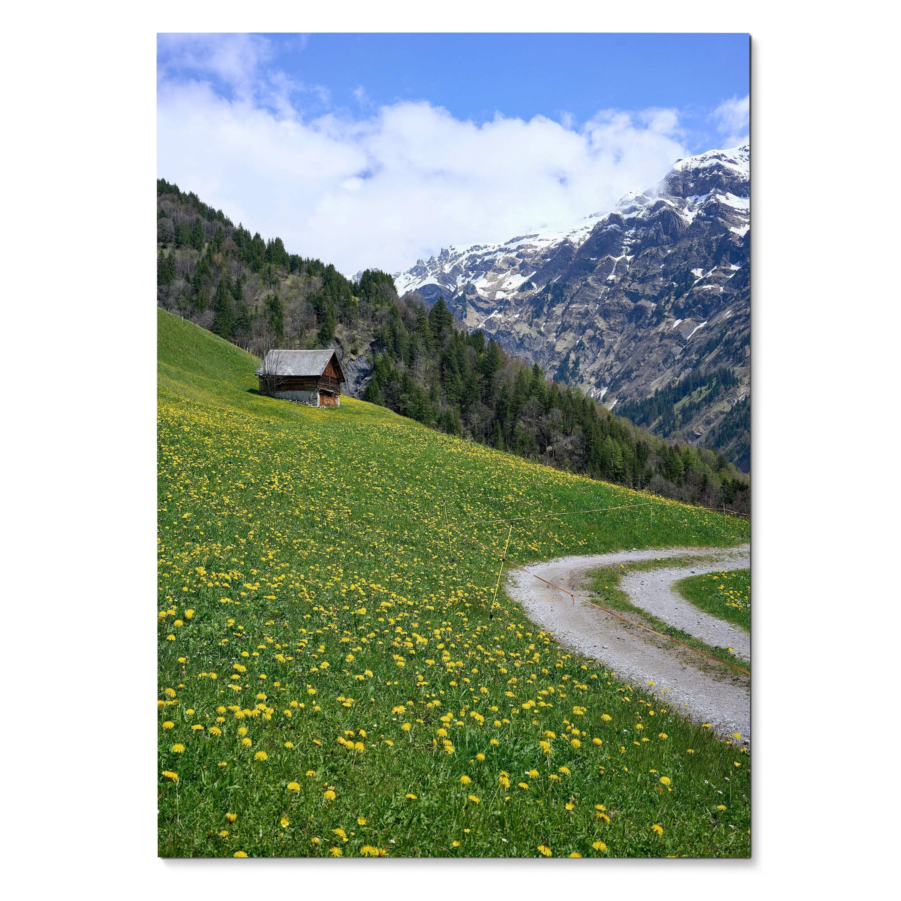 Vertical poster wall art featuring a green hillside with yellow flowers, a small cabin, and snow-capped mountains under a.