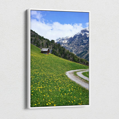 Canvas wall art featuring a green meadow with yellow flowers, winding path, and snow-capped mountain background.