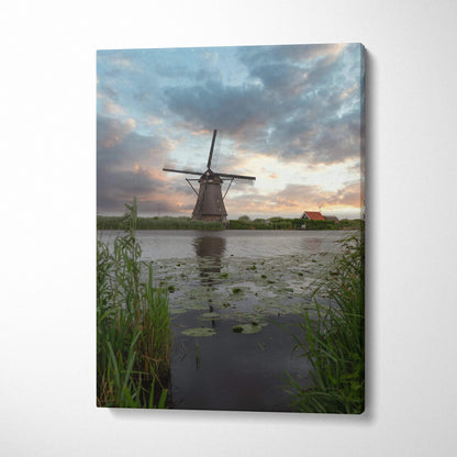 Canvas wall art featuring a windmill silhouette at sunset over a reflective pond with lily pads and grasses.