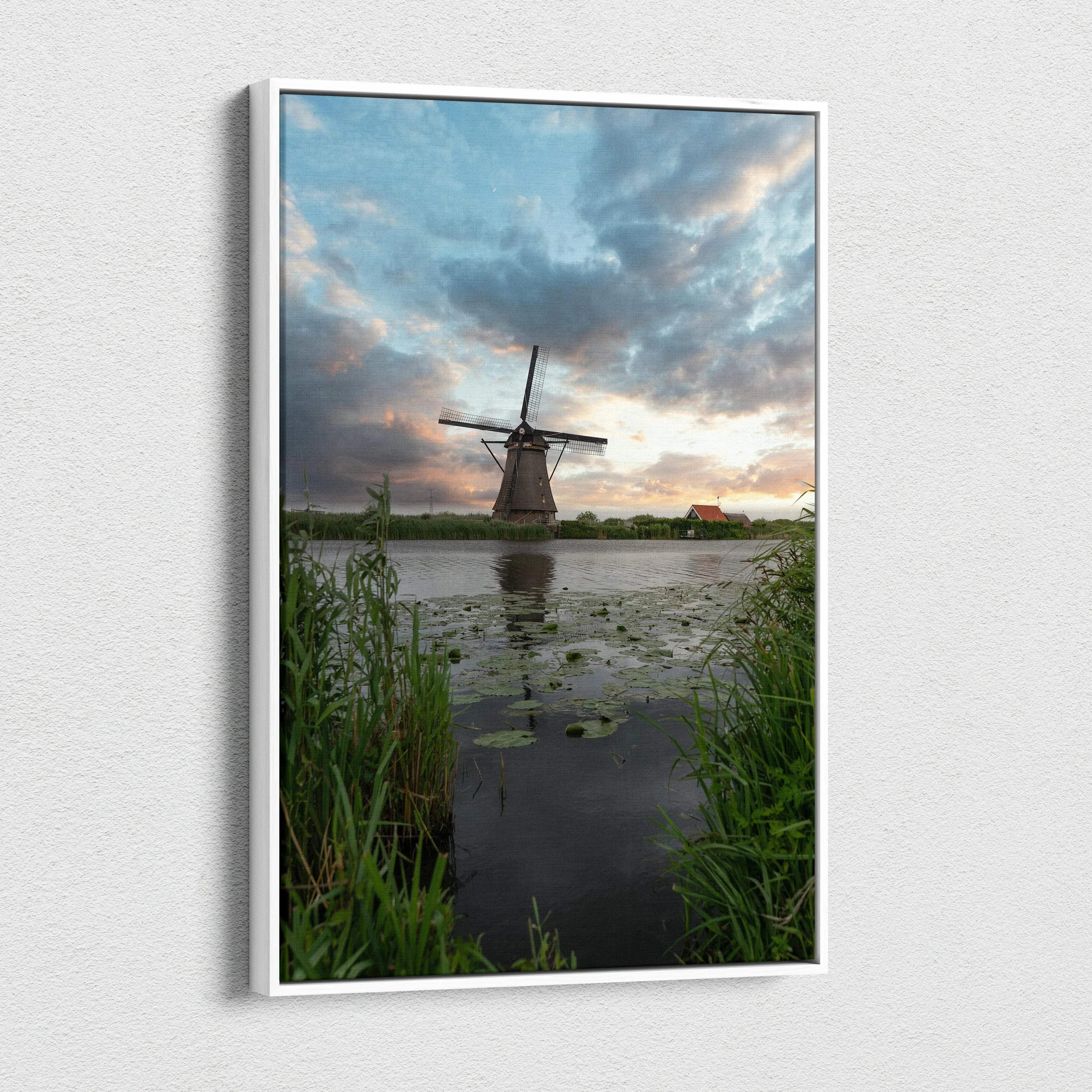 Vertical canvas wall art featuring a windmill at sunset with dramatic clouds over water and tall grass.
