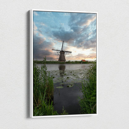 Vertical canvas wall art featuring a windmill at sunset with dramatic clouds over water and tall grass.
