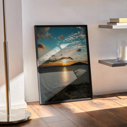 Vibrant ocean sunset poster with dramatic clouds and reflective water, framed wall art displayed on floor.