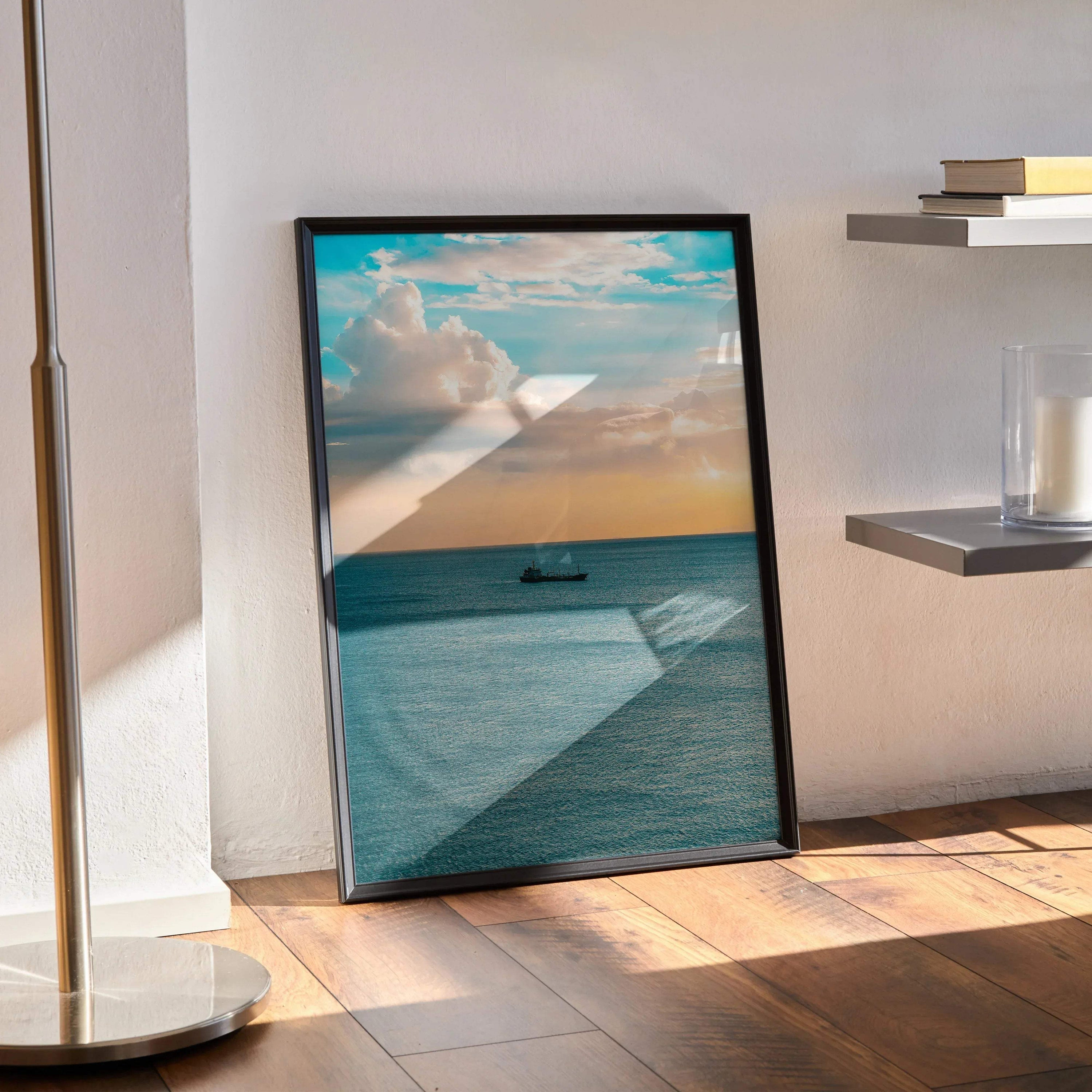 Ocean sunset poster with boat on calm water in black frame leaning on wall, vertical wall art.