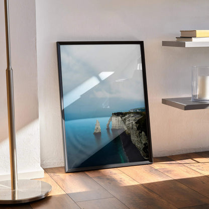Ocean beach nature poster with cliff and calm blue water, vertical wall art in black frame.