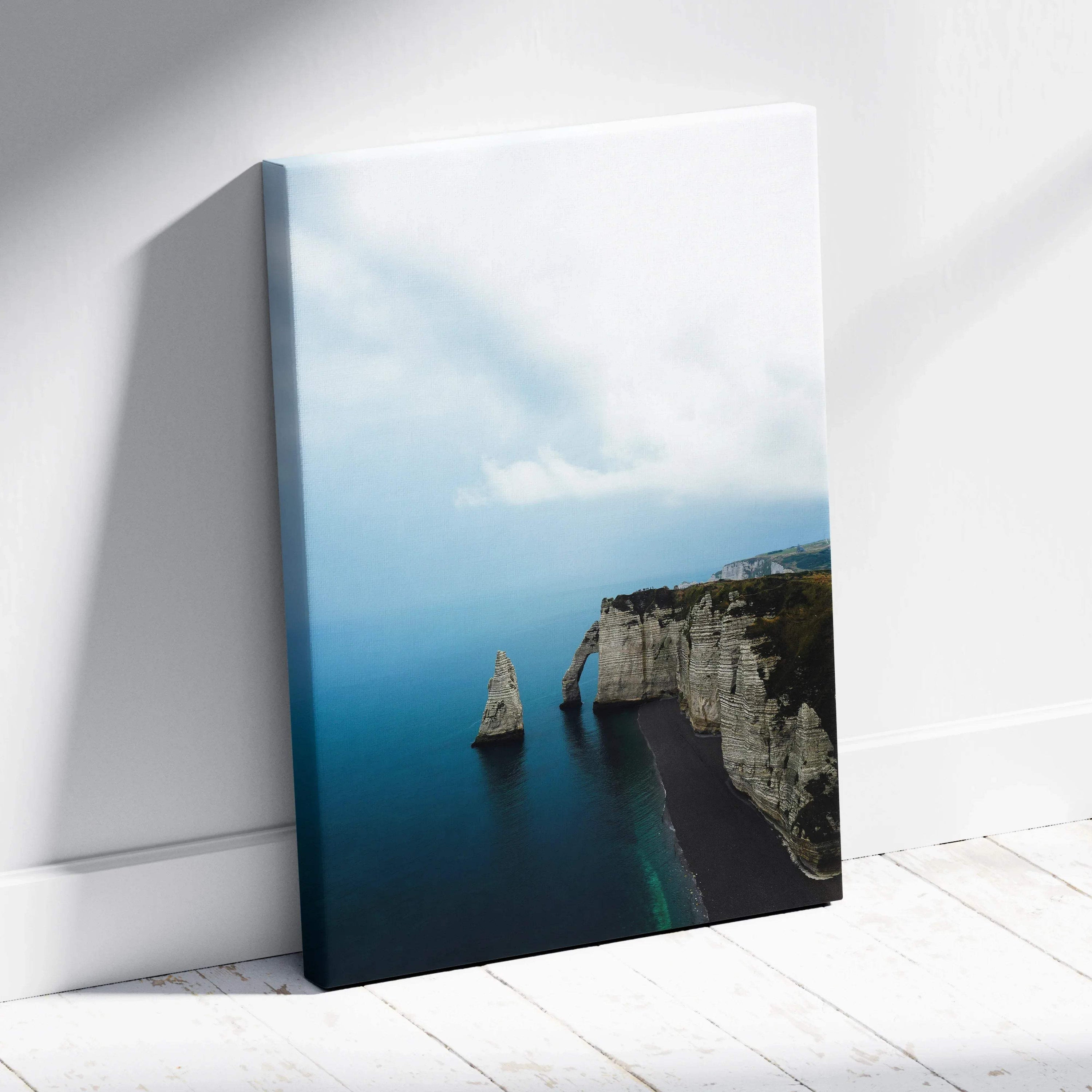 Vertical canvas wall art featuring serene blue ocean and rugged cliffside under a cloudy sky.