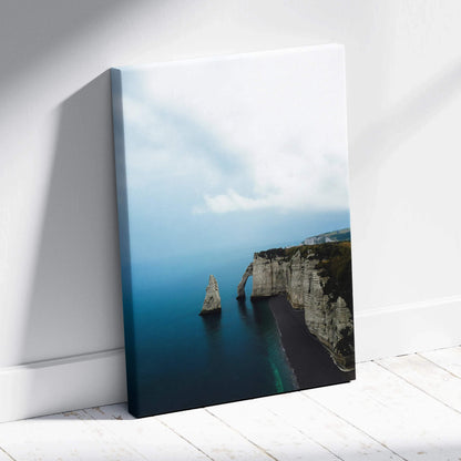 Vertical canvas wall art featuring serene blue ocean and rugged cliffside under a cloudy sky.