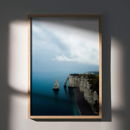 Vertical ocean beach wall art poster featuring dramatic cliffs and calm blue water under a cloudy sky.