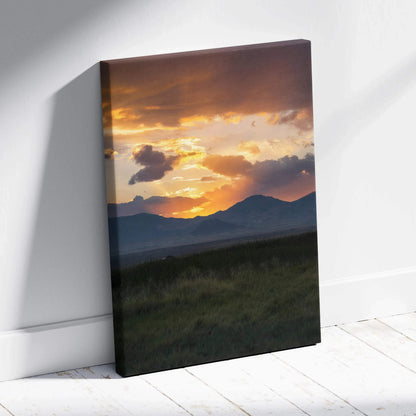 Canvas wall art of a vibrant mountain sunset with glowing orange and yellow clouds above dark silhouettes.