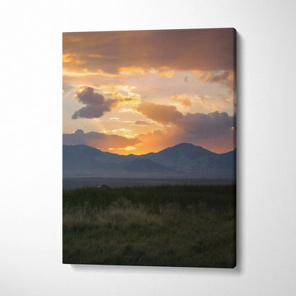 Canvas wall art featuring a vibrant sunset over mountain silhouettes with dark foreground grass.