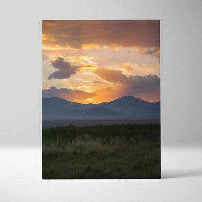 Vertical canvas wall art showing a vivid mountain sunset with orange and purple clouds over dark silhouette peaks.
