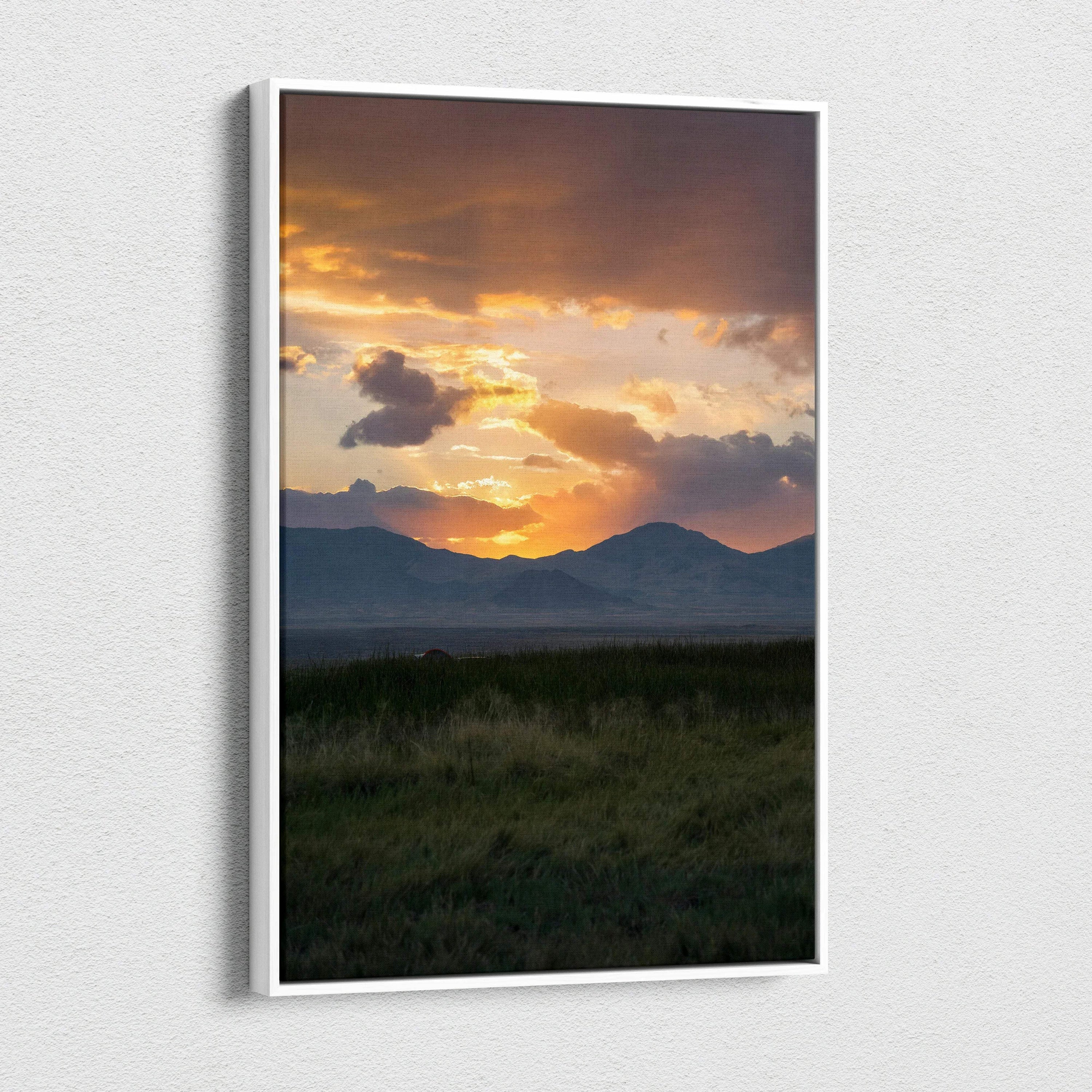 Vertical canvas wall art of a vivid sunset casting golden light over mountain silhouettes and grassy foreground.