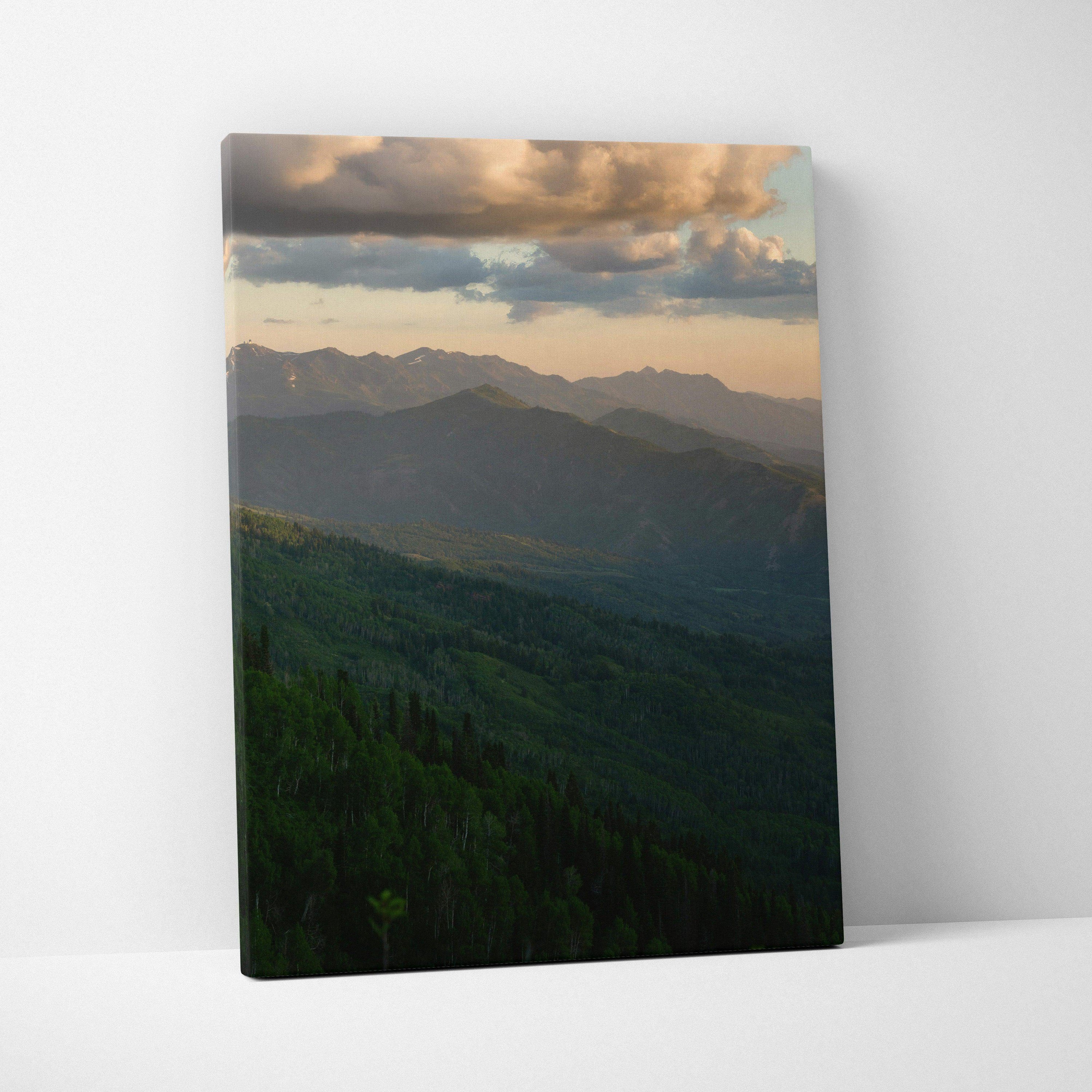 Canvas wall art featuring a serene mountain landscape at sunset with warm clouds and green forested hills.
