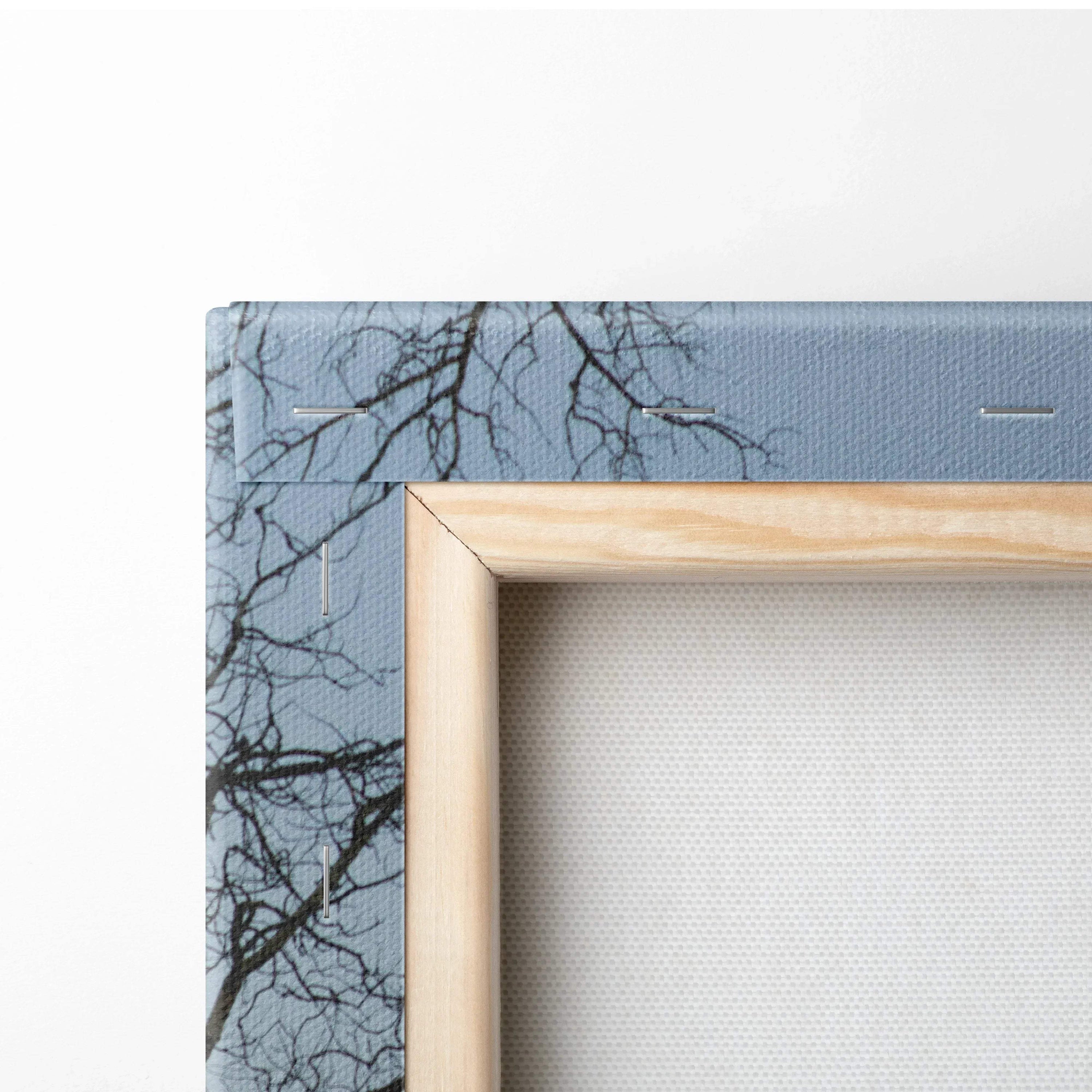 Canvas wall art with wooden frame featuring a mountain landscape and tree branches against a blue sky.