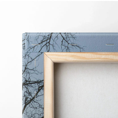 Canvas wall art with wooden frame featuring a mountain landscape and tree branches against a blue sky.