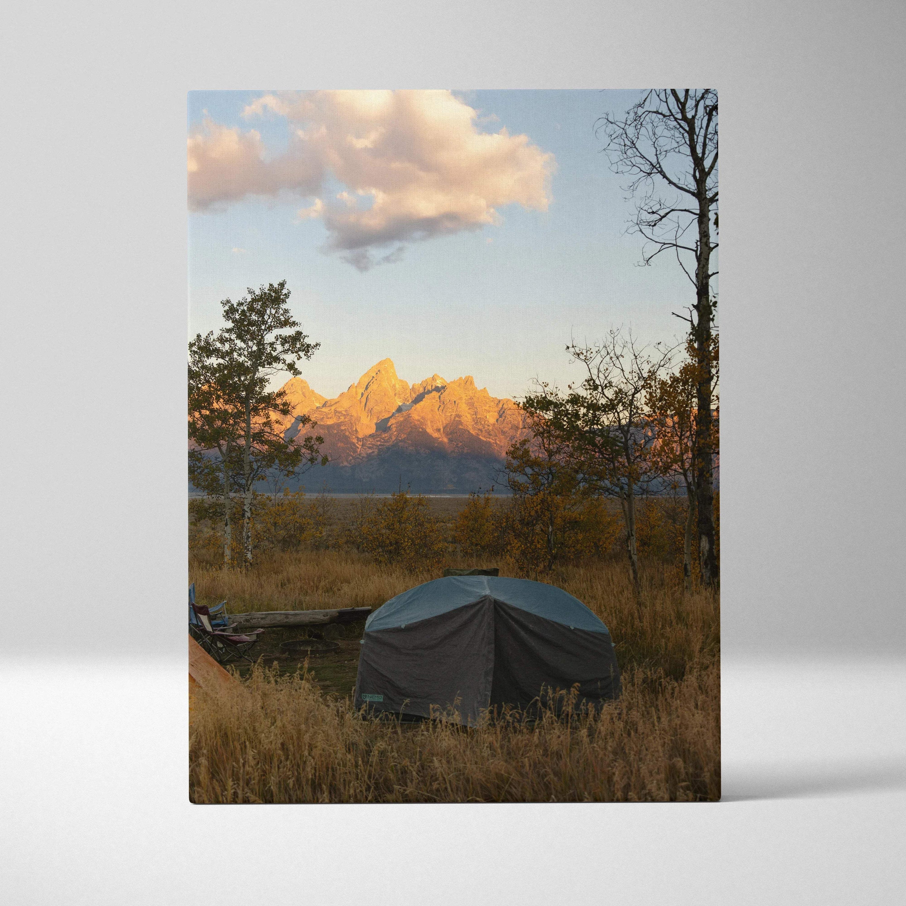 Vertical canvas wall art depicting a tent in a grassy field with mountains lit by sunset light.