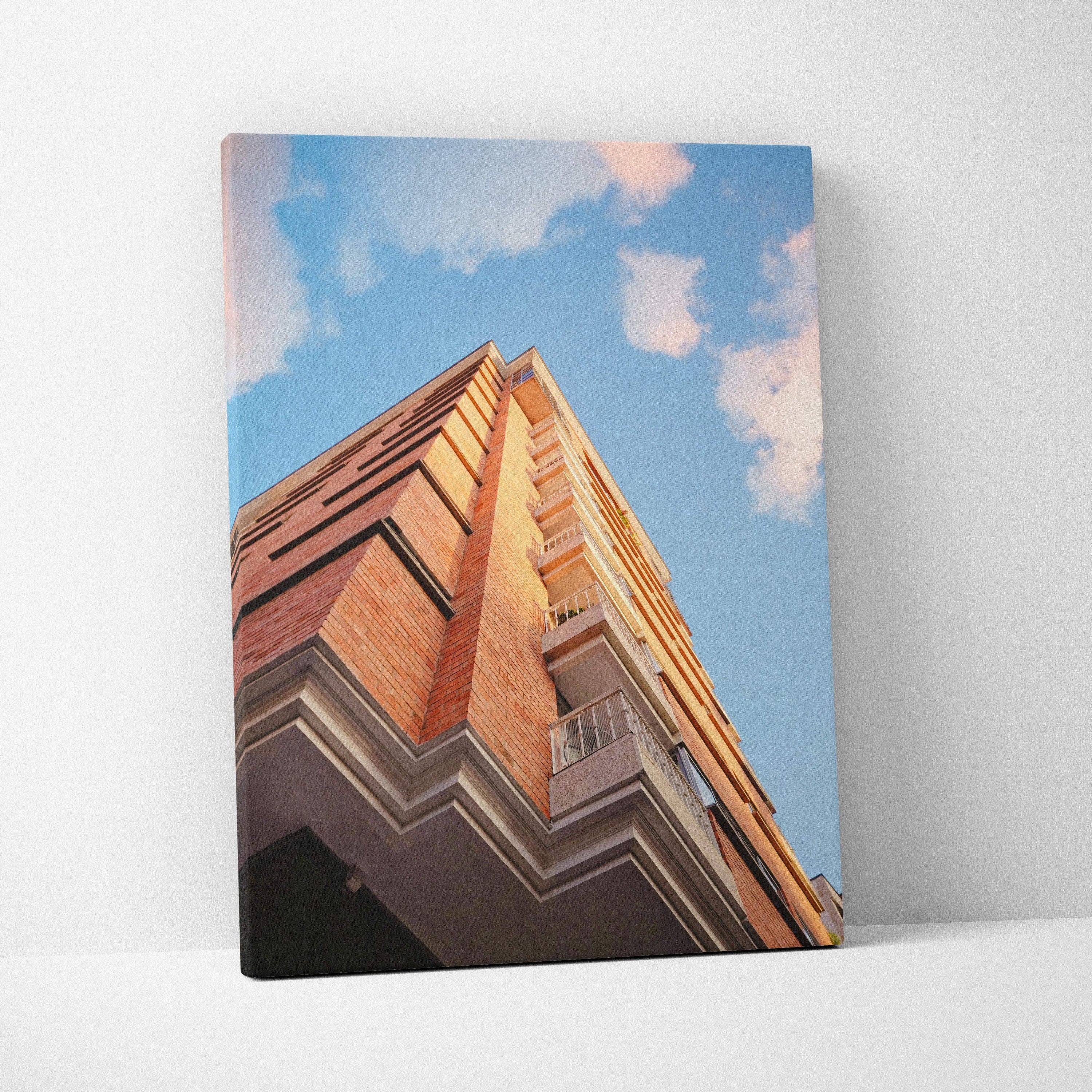 Vertical canvas wall art featuring a red brick urban building against a blue sky with clouds.