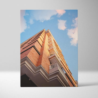 Urban brick building artwork on canvas wall art with blue sky and clouds backdrop.