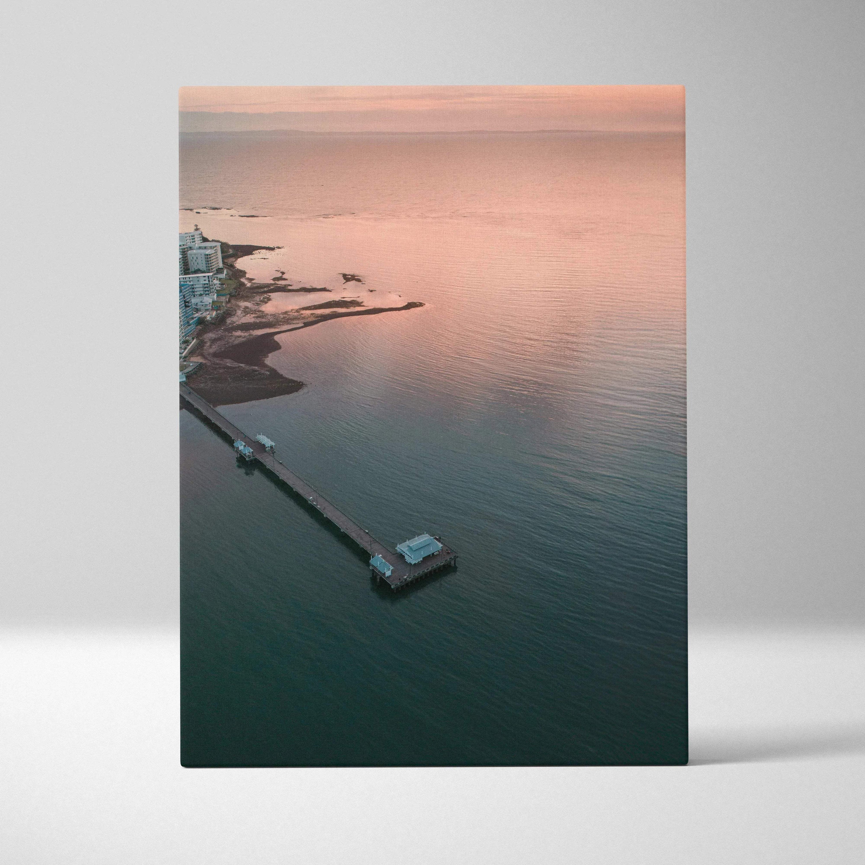 Vertical canvas wall art featuring a tranquil ocean sunset over a pier and calm water.