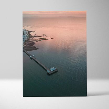 Vertical canvas wall art featuring a tranquil ocean sunset over a pier and calm water.