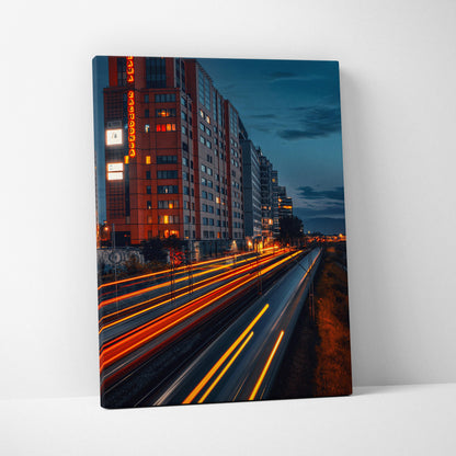 Vertical canvas wall art featuring vibrant urban cityscape with light trails and illuminated buildings at dusk.